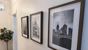 Tres fotografías en blanco y negro enmarcadas en una pared, una planta en maceta y una puerta.