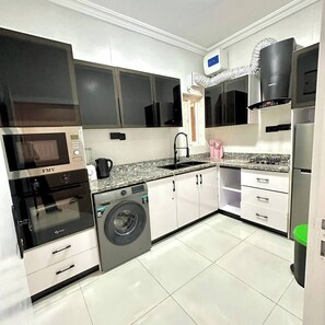 A modern kitchen with white cabinets, a built-in oven, a washing machine, and a sink.