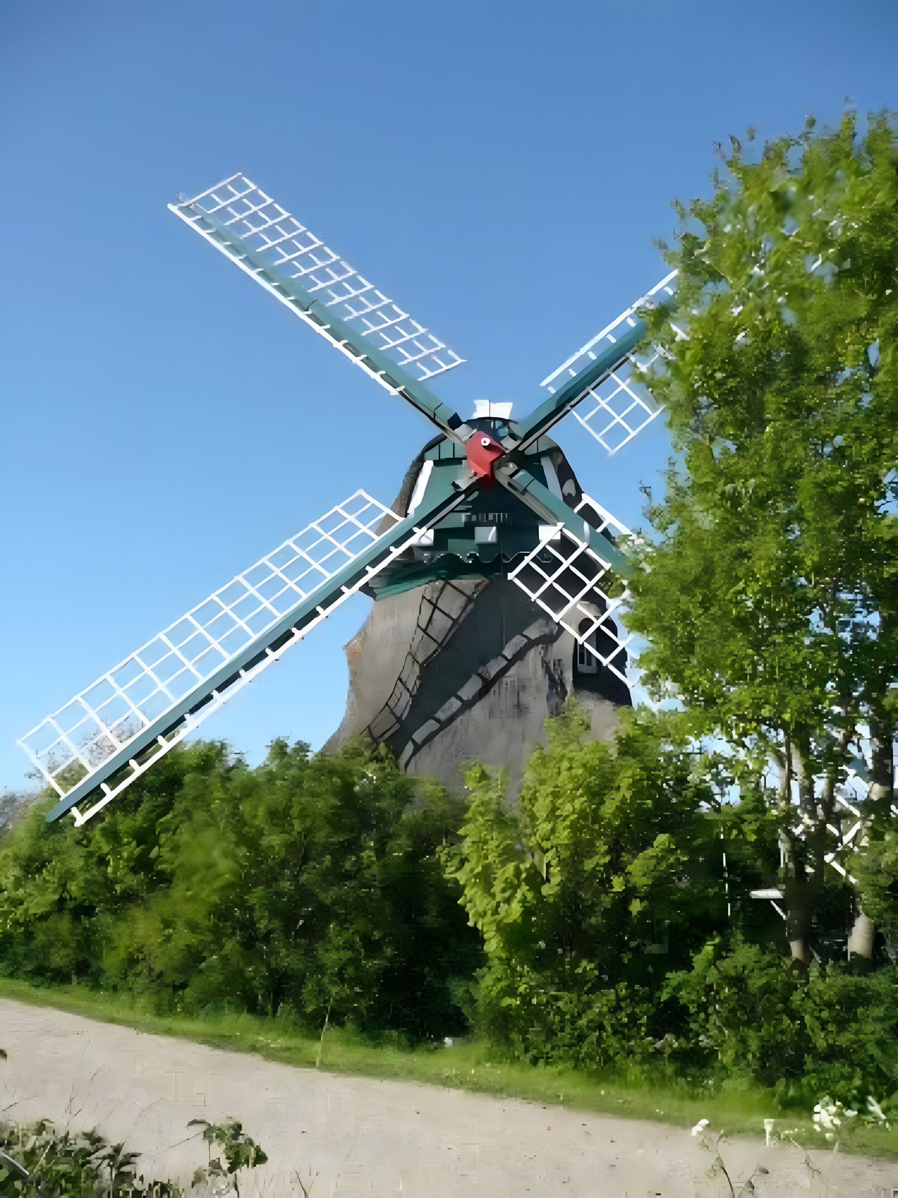 Un moulin à vent doté de quatre grandes pales, entouré de verdure.