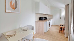 A modern kitchen with white cabinets, a microwave, and a washing machine. There is a dining area with a table and chairs. - Charming house -2BR-4P- Ivry-sur-seine (Ivry-sur-Seine)