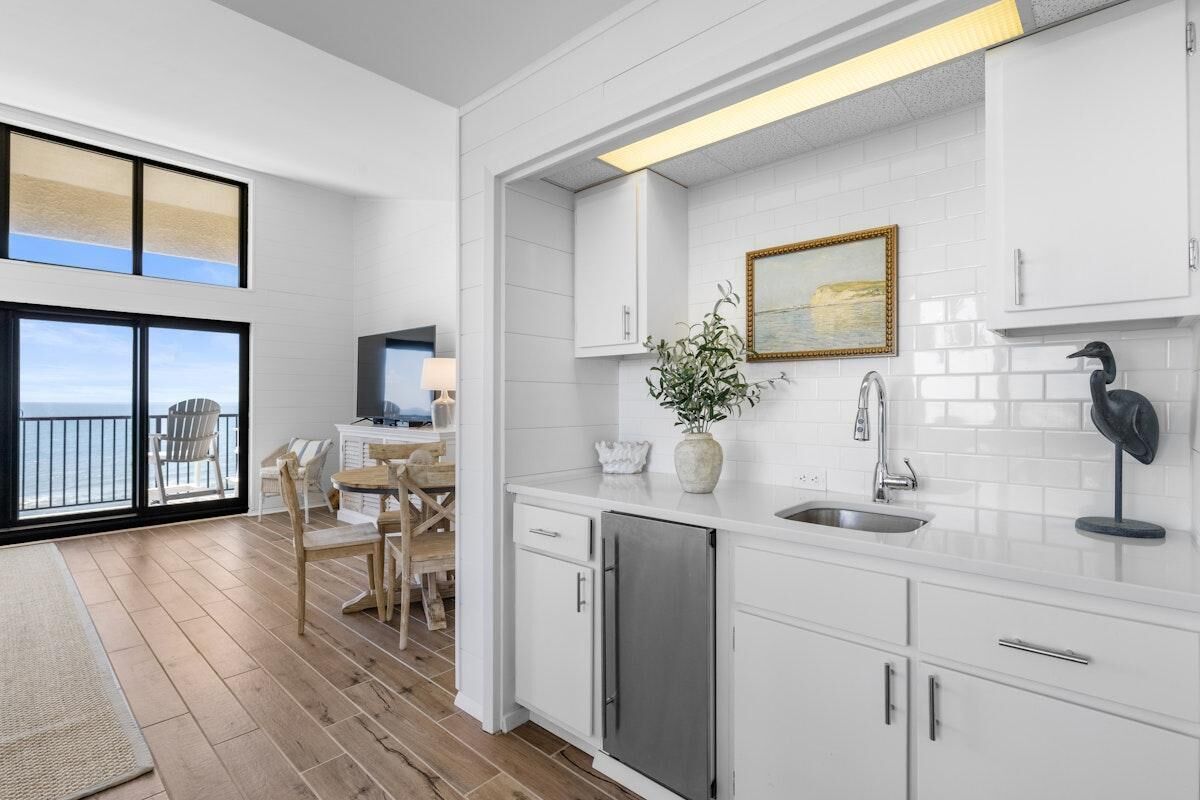 A modern kitchen with white cabinets, a stainless steel sink, and a dining area with wooden chairs.