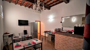 A dining area with tables set for four, a television mounted on the wall, a refrigerator, and a brick counter with a mirror. - Le Stanze dei Ghibellini (Florence)