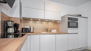 A modern kitchen with white cabinets, a wooden countertop, a coffee maker, a kettle, and a built-in oven. - Beachfront apartment for two people on the pier (Graal-Müritz)