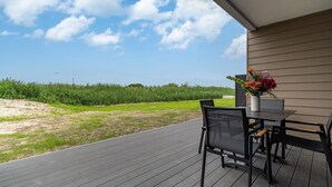 An outdoor patio with a table and chairs, a potted plant, and a view of a grassy field and trees. - Beachfront apartment for two people on the pier (Graal-Müritz)