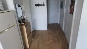 Een smalle gang met houten vloer, een witte deur aan het einde en een kleed in het midden.