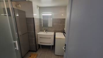 A compact bathroom with a glass shower enclosure, a sink with a mirror, and a small refrigerator.