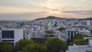 Un paisaje urbano con una colina destacada al fondo, numerosos edificios y un cielo despejado.