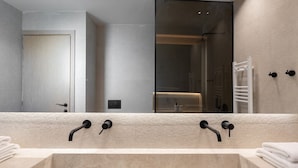 Un baño moderno con un lavamanos beige grande, dos grifos negros y un espejo amplio.