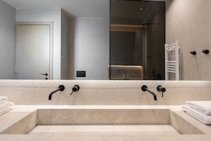 Un baño moderno con un lavabo beige grande, dos grifos negros y un espejo amplio.