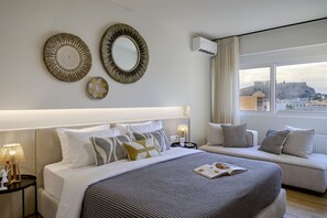 A modern hotel room with a large bed, a sofa, decorative wall mirrors, and a view of a historic building. - Acropolis Terraces in Athens (Athens)