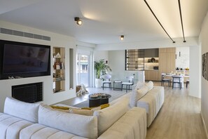 A modern living room with a TV, seating area, and a kitchen in the background.