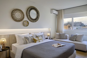 Ett modernt hotellrum med en stor säng, en soffa, dekorativa väggspeglar och utsikt över en historisk byggnad.