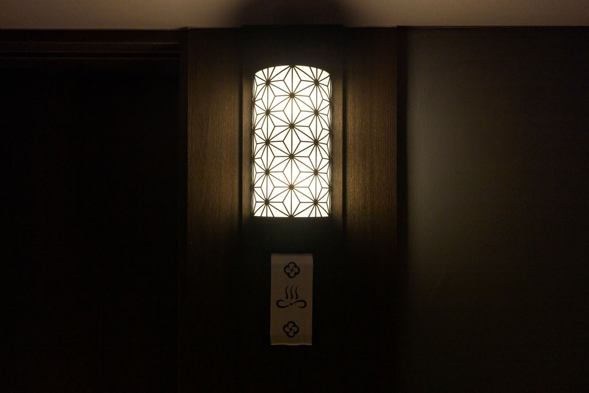 Una puerta de madera oscura con un ventanal de diseño geométrico y un letrero con un símbolo.