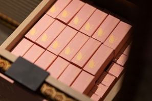 Un gros plan d’une boîte en bois contenant plusieurs petites boîtes roses ornées de motifs de feuilles jaunes.