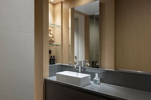 Une salle de bain moderne avec un grand miroir, un lavabo blanc et une étagère en verre où sont rangés les articles de toilette.