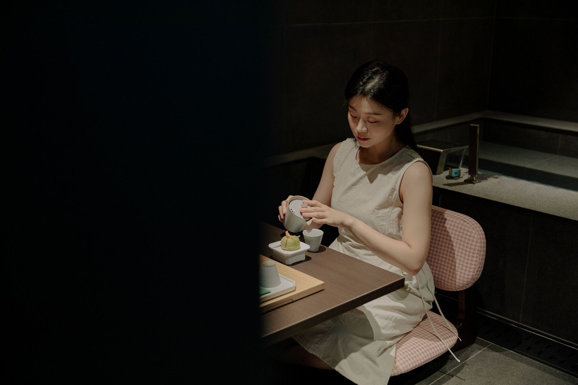 A person seated at a table with a cup and saucer, a small bowl, and a spoon.
