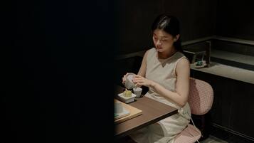 A person seated at a table with a cup and saucer, a small bowl, and a spoon.