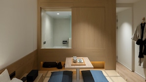 Een moderne hotelkamer met een houten scheidingswand, een klein tafeltje met dienblad en een spiegel die de badkamer weerkaatst.