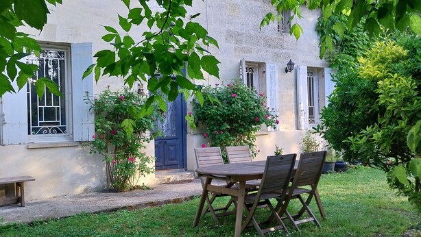A courtyard with a wooden table and chairs, a blue door, and a white building with windows. - Guest Room “La Lagune” with Shared Terrace, Private Garden and Wi-Fi (Saint-André-de-Cubzac)