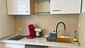 A kitchen with white cabinets, a red coffee maker, a kettle, a toaster, and a sink with a dish rack. - Apartment in Trier With Parking (Trier)