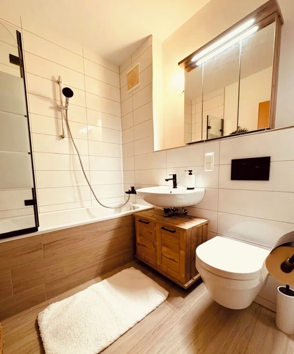 Un baño moderno con ducha, lavamanos, inodoro y un mueble de madera.
