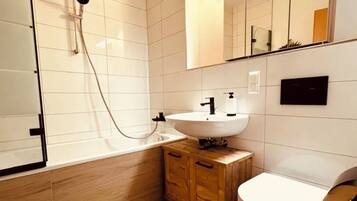 Un baño moderno con ducha, lavamanos, inodoro y un mueble de madera.