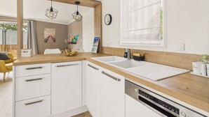 Une cuisine moderne avec des armoires blanches, un plan de travail en bois, un lave-vaisselle encastré et des luminaires suspendus.