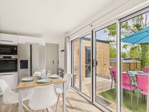 Eine moderne Küche mit Einbaugeräten, ein Essbereich mit Holztisch und weißen Stühlen sowie eine Glastür, die auf eine Terrasse im Freien mit einem blauen Sonnenschirm führt.