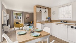 Une cuisine moderne avec des meubles blancs, un plan de travail en bois et un coin repas avec une table dressée pour deux personnes.