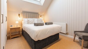 Une chambre avec un puits de lumière, un lit avec des oreillers, une table de chevet, une chaise et un radiateur.