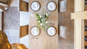 Un coin repas avec une table en bois dressée pour quatre personnes, entourée de chaises rembourrées, et un vase avec des fleurs posé sur la table.