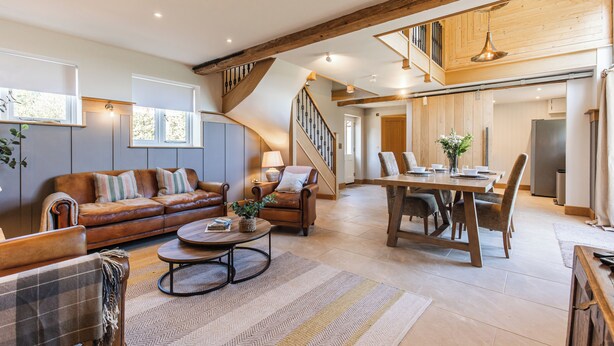 Un vaste espace de vie comprenant un canapé en cuir marron, une table à manger en bois et un escalier menant à un niveau supérieur.