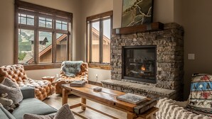 Una sala de estar acogedora con chimenea de piedra, sofá de cuero y vistas a las montañas a través de amplios ventanales.