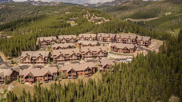 Un complejo turístico con varias edificaciones de estilo chalet dispuestas en un diseño semicircular, rodeado de un bosque denso y montañas al fondo.