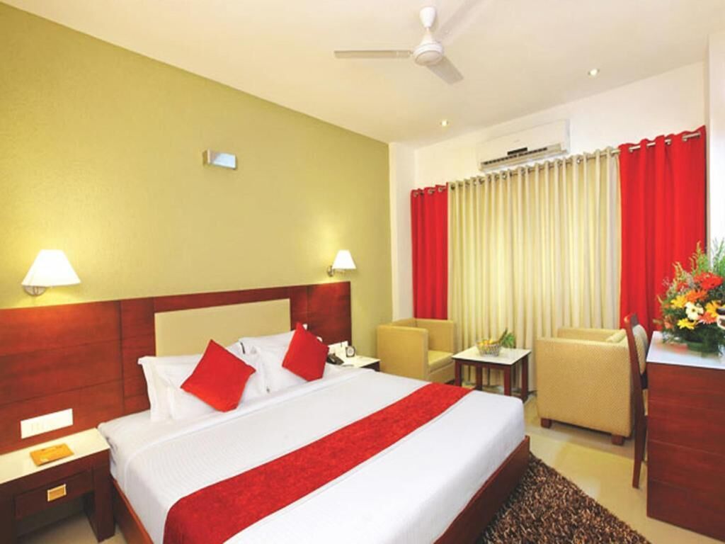 A hotel room with a large bed, two bedside tables, a desk, a chair, and a red and white curtain.