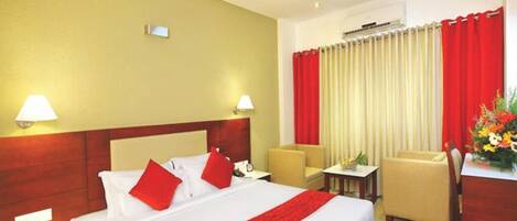 A hotel room with a large bed, two bedside tables, a desk, a chair, and a red and white curtain.