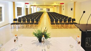 Een vergaderzaal met rijen stoelen, een spreekgestoelte en een tafel met waterflesjes en een plant.