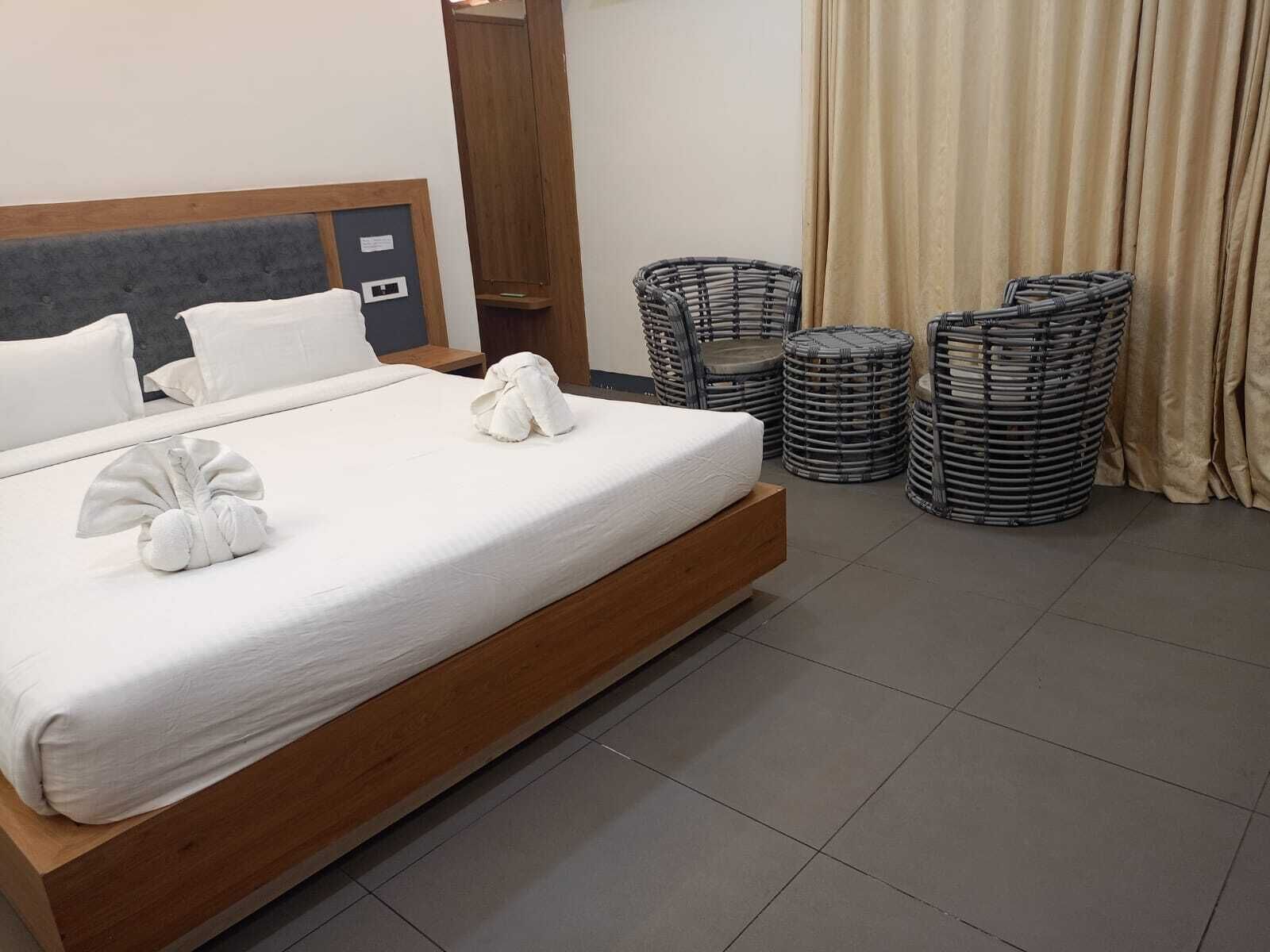 Een netjes opgemaakt bed met witte lakens en handdoeken, een houten hoofdbord, een klein nachtkastje en een rieten stoel.