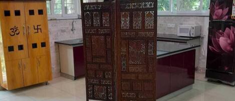 A room with a tiled floor, a wooden cabinet with symbols, a decorative partition, a microwave, and a refrigerator with a floral design.