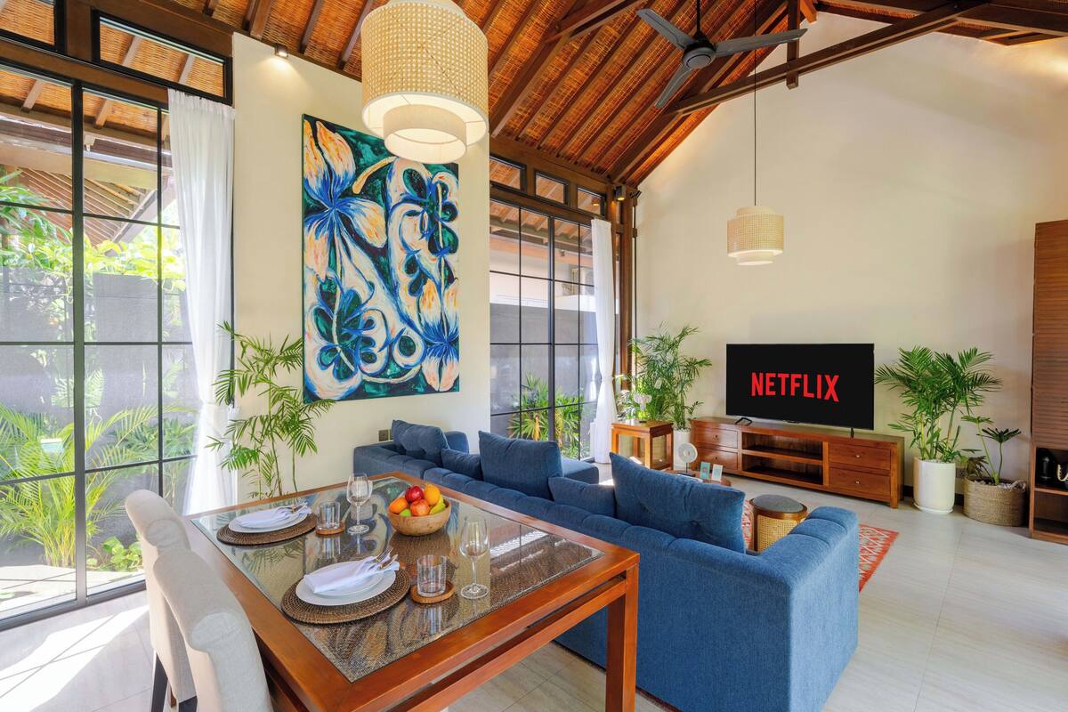 A modern living room with a large sofa, a dining table set for four, and a TV displaying 'NETFLIX'.