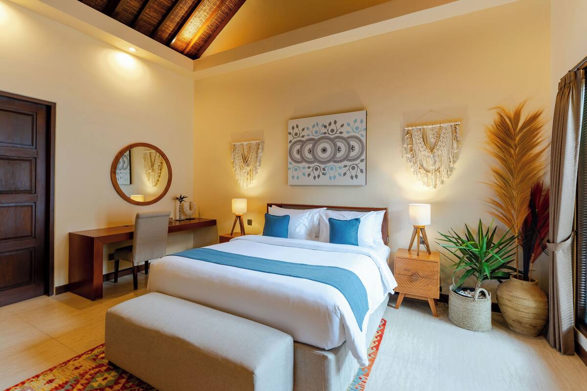 A bedroom with a large bed, bedside tables, a desk, a chair, and decorative wall art.