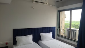 Une chambre d’hôtel avec deux lits, un ventilateur de plafond, un appareil de climatisation, une fenêtre donnant sur un espace verdoyant et une rambarde de balcon.