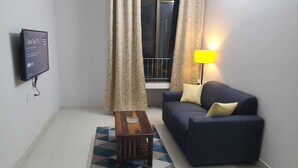 Un salon avec un canapé, une table basse, un téléviseur et une fenêtre avec des rideaux.