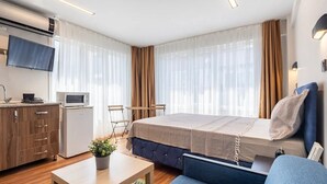 A compact hotel room with a bed, a small kitchenette, a TV, and a seating area with a sofa and chairs.