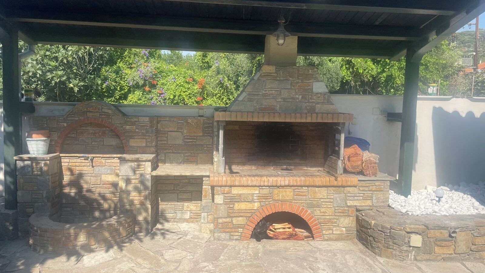 Un espace barbecue extérieur en pierre, doté d’une cheminée, d’un foyer et d’un coin salon abrité.