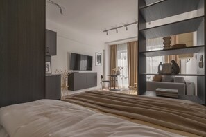 Ein modernes Hotelzimmer mit einem großen Bett, einem an der Wand montierten Fernseher, einer Sitzecke mit Tisch und Stühlen sowie einem Bücherregal.
