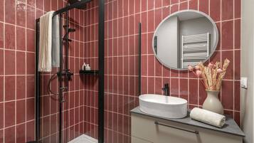 A modern bathroom with a glass-enclosed shower, a round mirror, a white sink, and a vase with dried flowers.