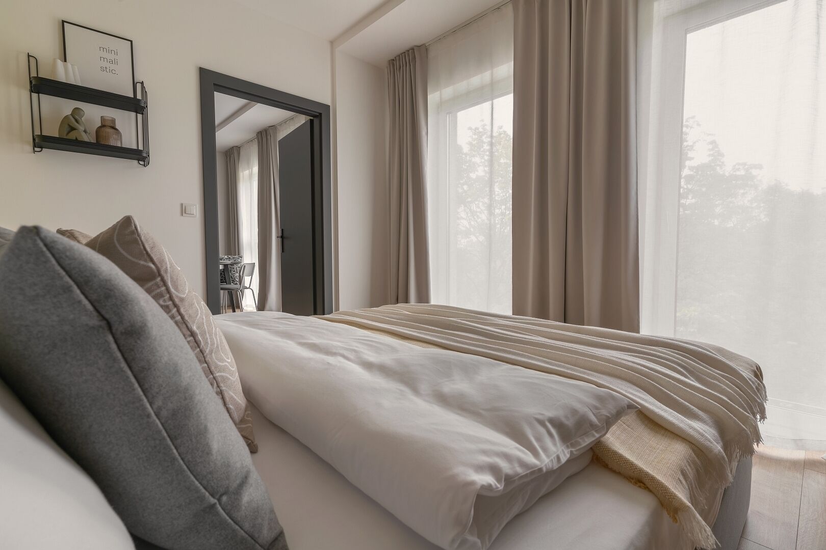 Quarto com cama, mesa de cabeceira, espelho e janela com cortinas.