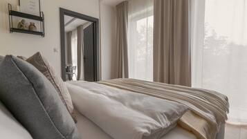 Quarto com cama, mesa de cabeceira, espelho e janela com cortinas.