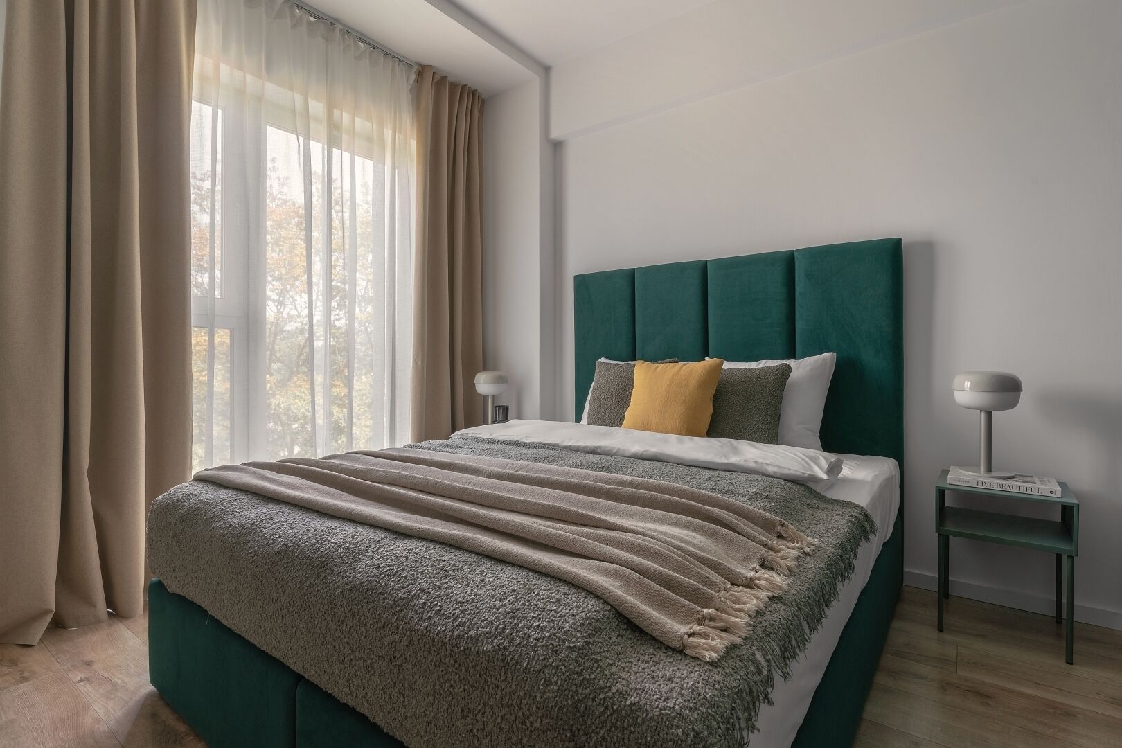 A modern bedroom with a large bed, a headboard, two bedside tables, and a window with curtains.